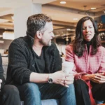 Three C12 members sitting on a couch talking in a hotel lobby with coffee.